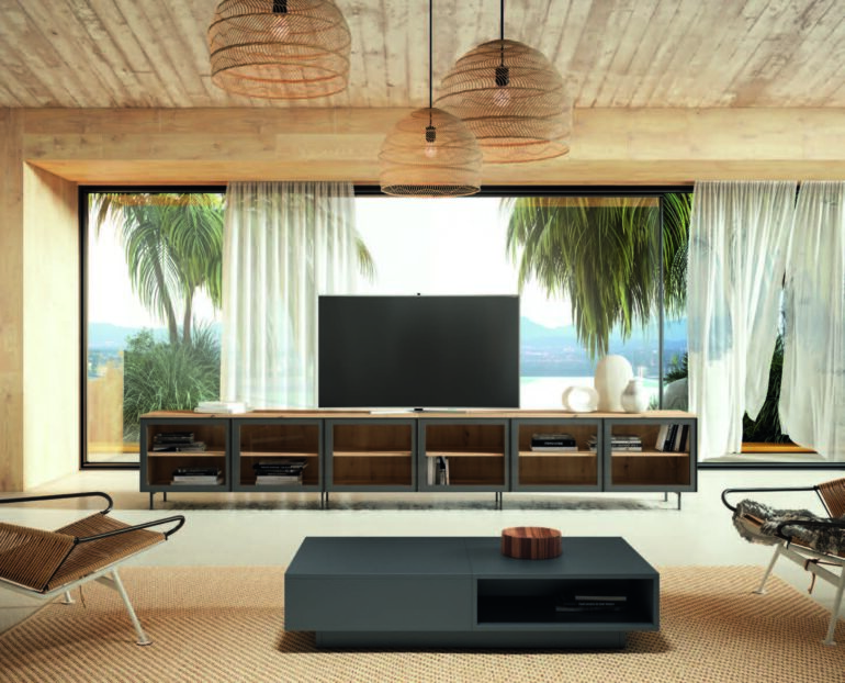 Living room with three woven pendant lamps above a dark media console and flat-screen TV, large glass doors show a tropical outdoor view.